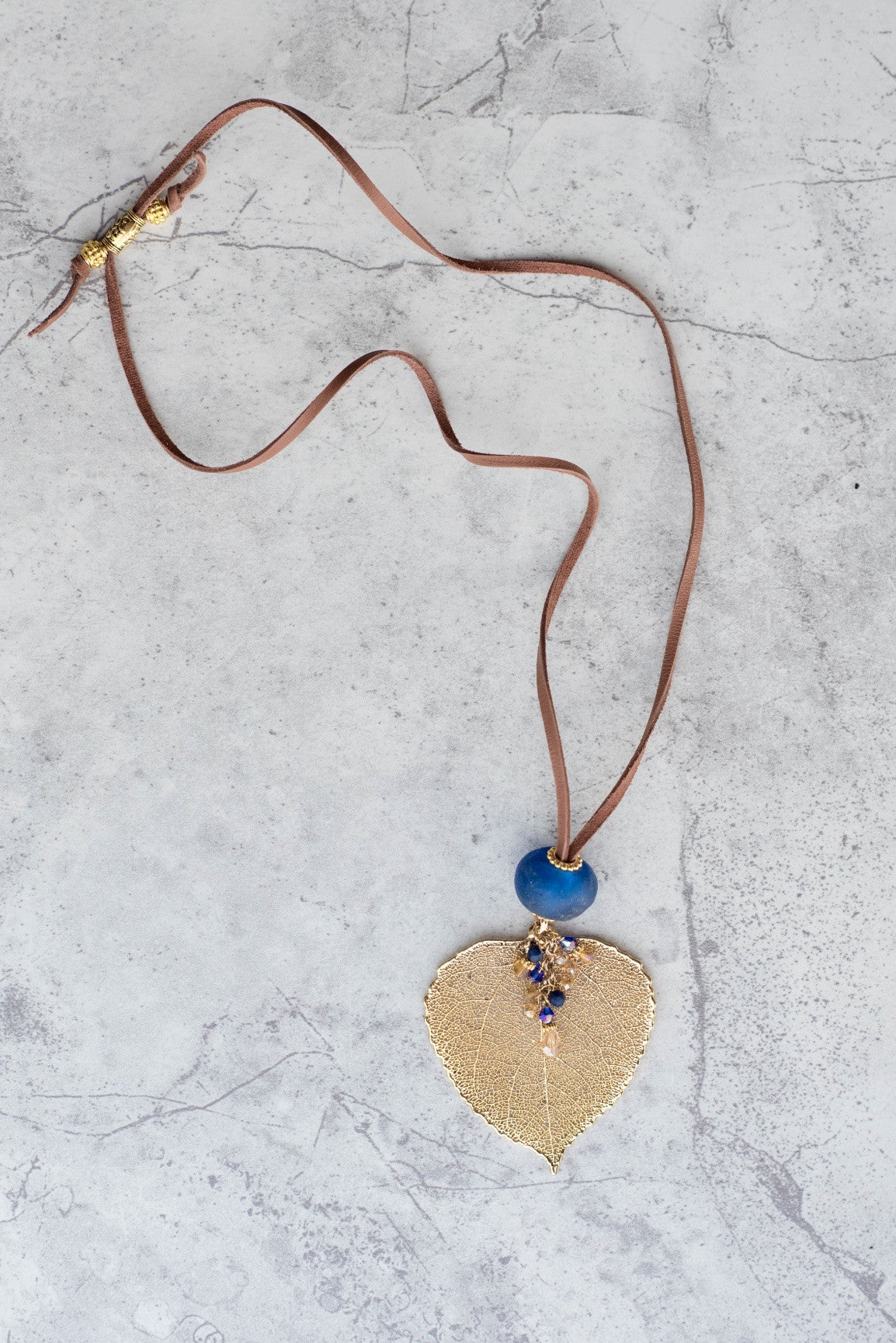 Single re-cycled African glass bead with a large Gold Aspen leaf finished with a stunning crystal dangle. Deerskin leather
