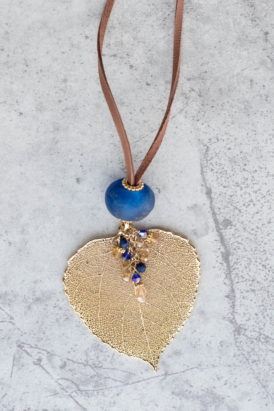 Single re-cycled African glass bead with a large Gold Aspen leaf finished with a stunning crystal dangle. Deerskin leather