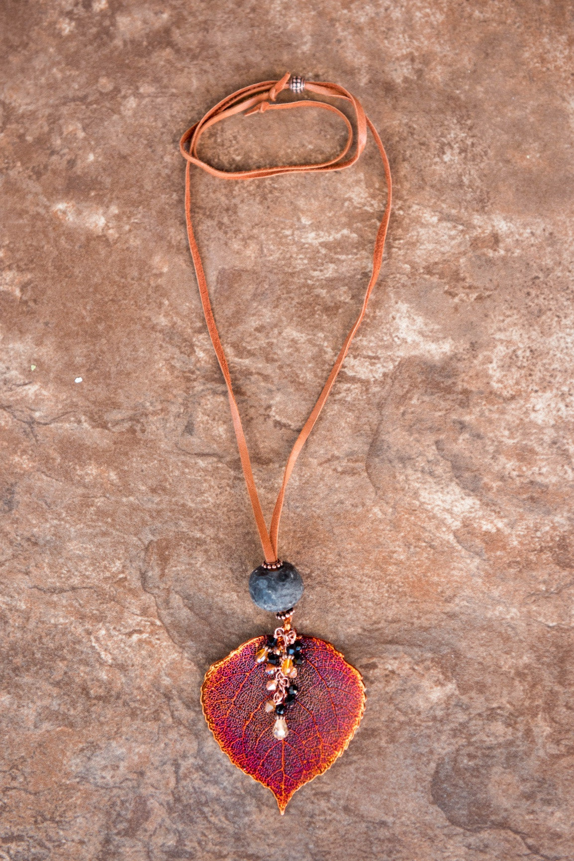 Single re-cycled African glass bead with a large copper Aspen leaf finished with a stunning crystal dangle. Deerskin leather